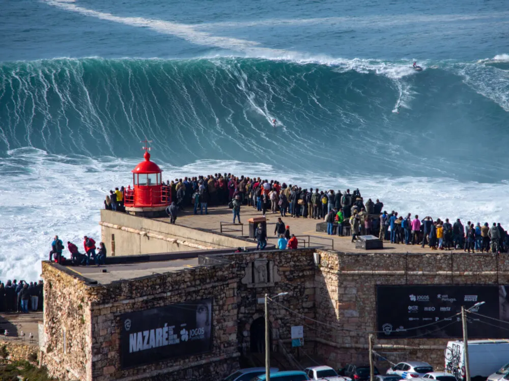 Giant wave being watched by onlookers in one of the best places to visit in Portugal, Nazare