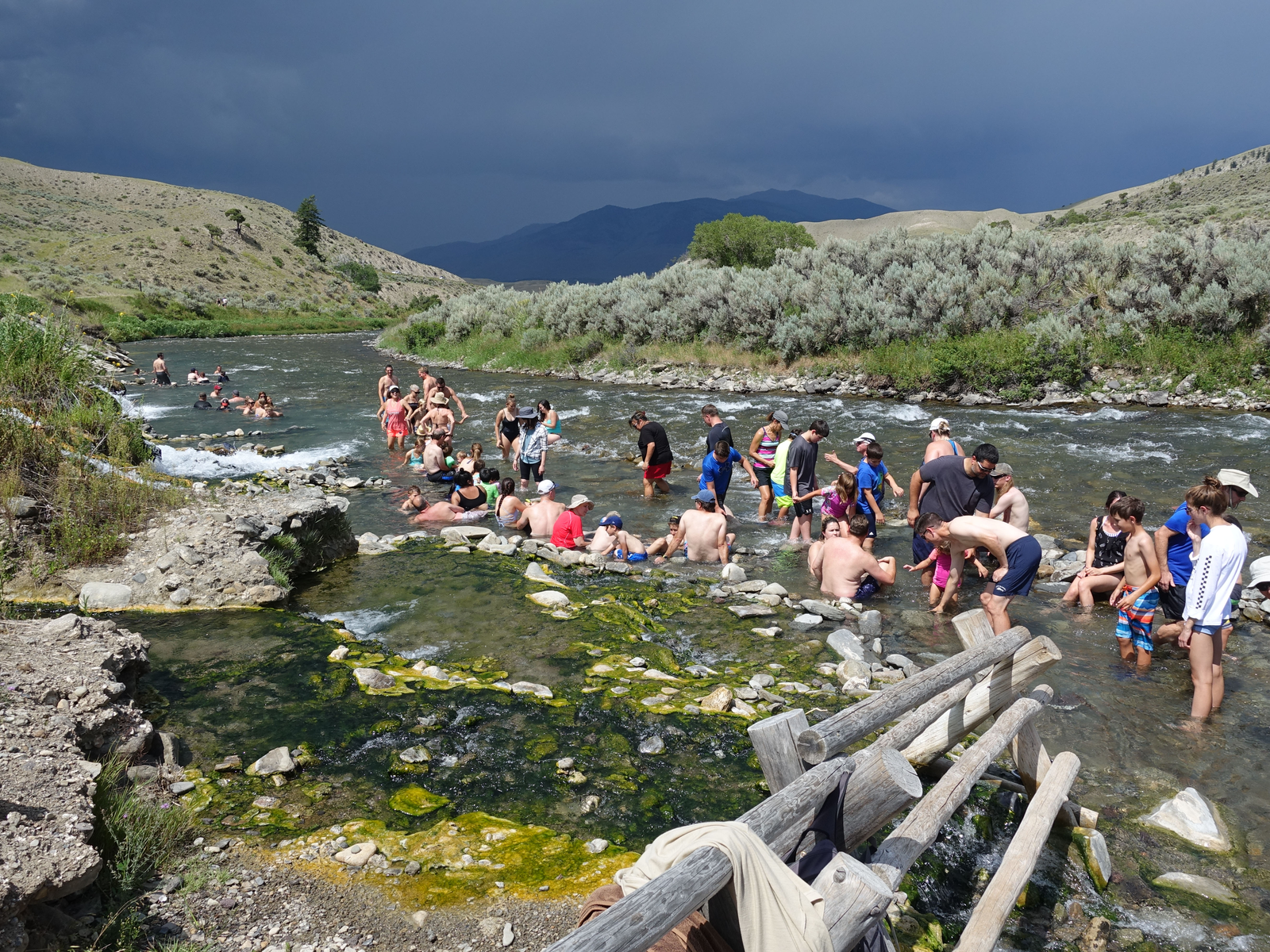 An excited group of tourist dipping at the iconic Boiling River, one of the best things to do in Montana, with algae covered rocks