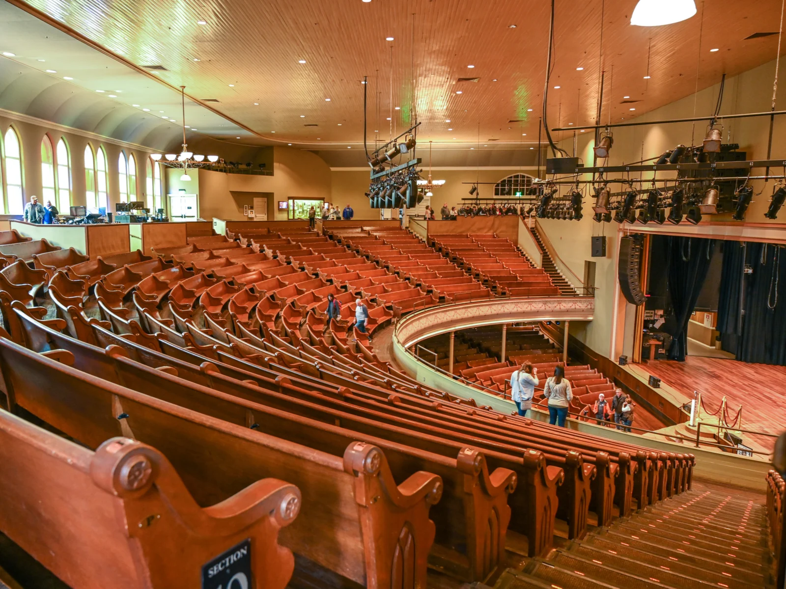 Spacious interior of the well known Ryman Auditorium consisting rows of long wooden chairs and hanging spotlights, photographed from the upper section as a piece on one of the best things to do in Tennessee