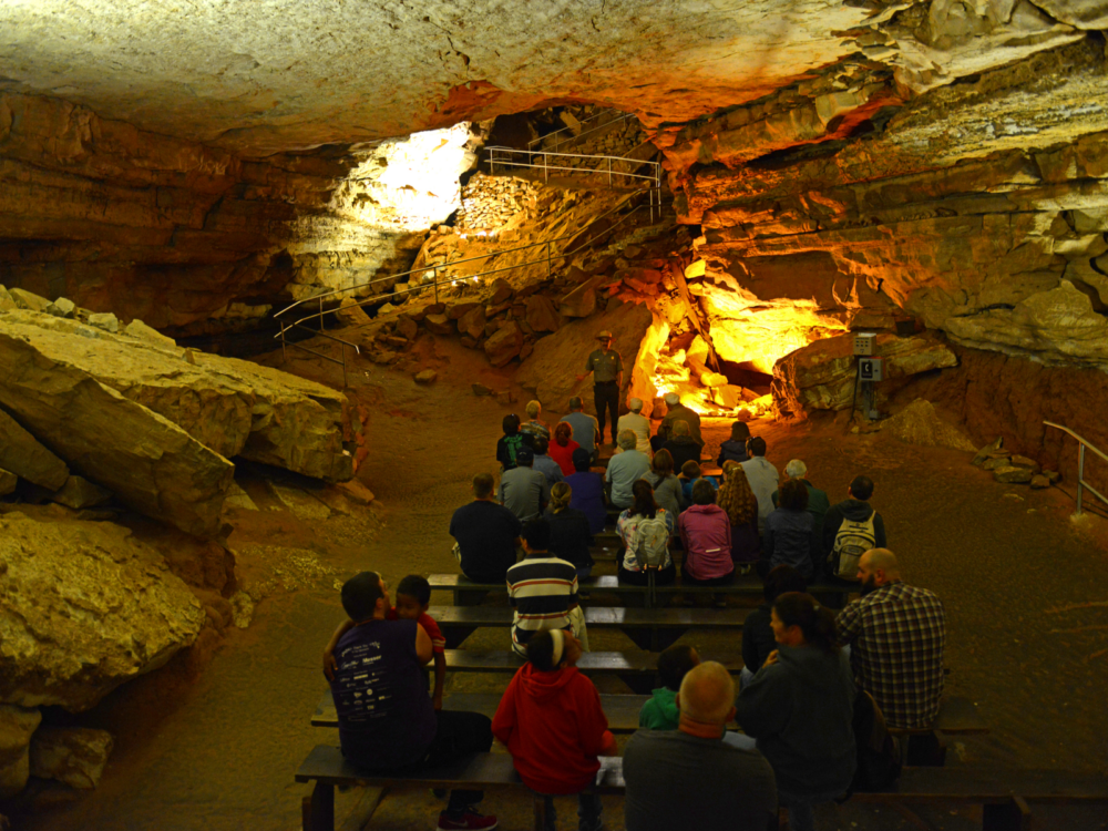 Tourists sitting down on benches while listening to the tour guide, one of the best things to do in Kentucky, speaking about Mammoth Cave National Park's history as one of UNESCO World Heritage Site