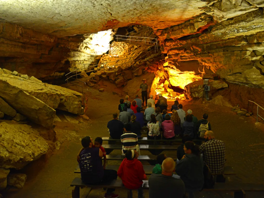 Tourists sitting down on benches while listening to the tour guide, one of the best things to do in Kentucky, speaking about Mammoth Cave National Park's history as one of UNESCO World Heritage Site