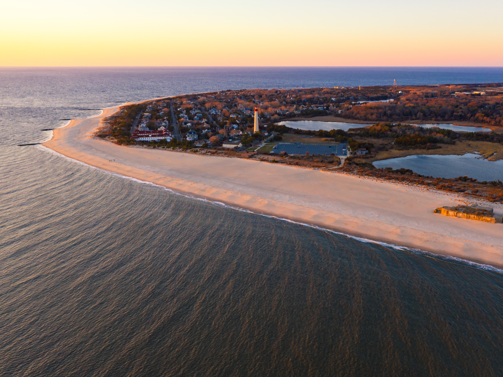 Aerial photo of a sunset over the calm waters and clear shore of Cape May Beach, as a piece on the best things to do in New Jersey
