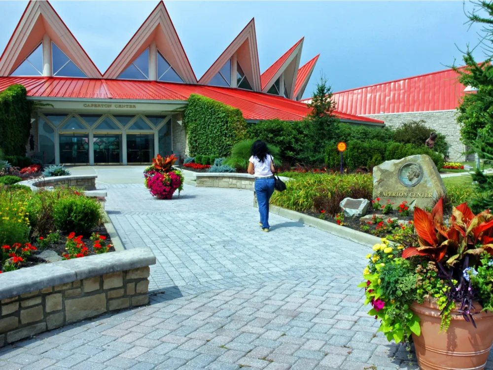 A woman carrying a black bag heading towards the Tamarack Center, with unique pointy roofing structure and beautiful exterior landscape, one of the best attractions in West Virginia