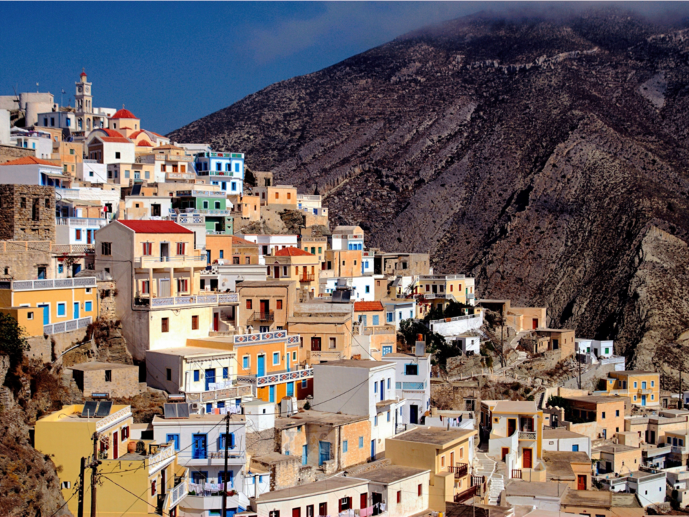 Colorful structures at sloppy Olympos Village in Karpathos Island, one of the best places to visit in Greece, contrasted by a large mountain