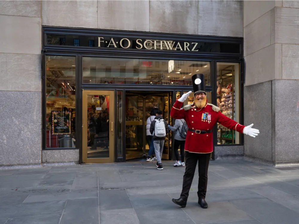 A man wearing a nutcracker toy costume gesturing 'salute', welcoming costumers in front of the famous FAO Schwarz in New York, one of the best toy stores in America