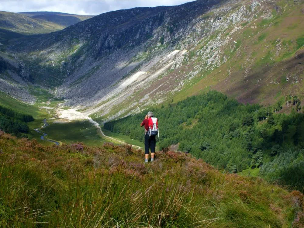 An adult hiker stopping to take photo of the scenic green landscape at Wicklow Mountains National Park, one of the best hikes in Ireland