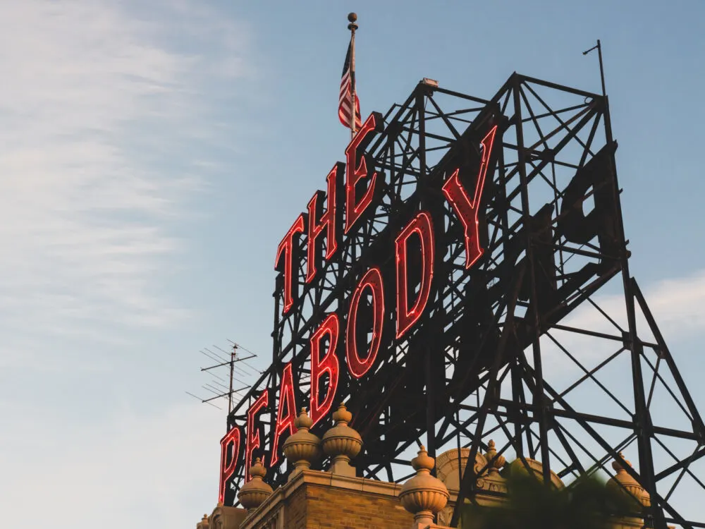 gigantic signage with red light outline on top of the building of Peabody Hotel and a US flag, seen as one of the best things to do in Tennessee