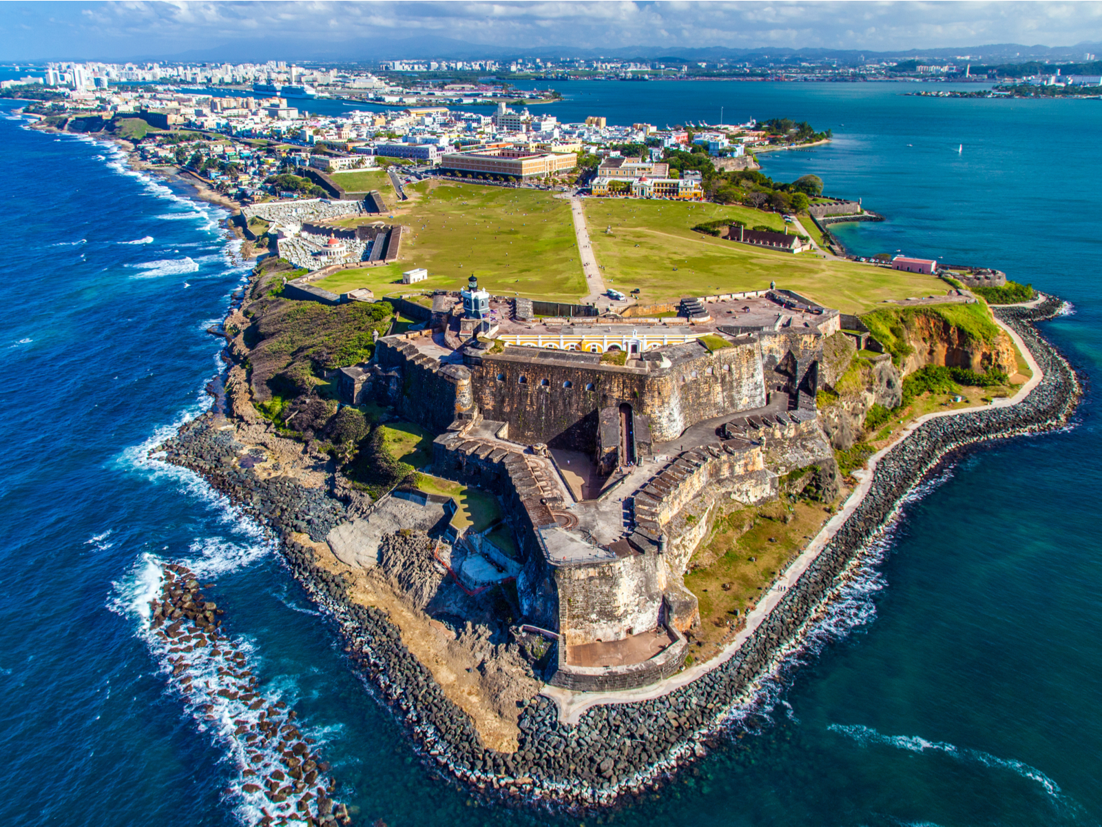 Stunning aerial photo of San Felipe del Morro with its rocky shoreline and San Juan's skyline in background, a must add item on things to do in Puerto Rico