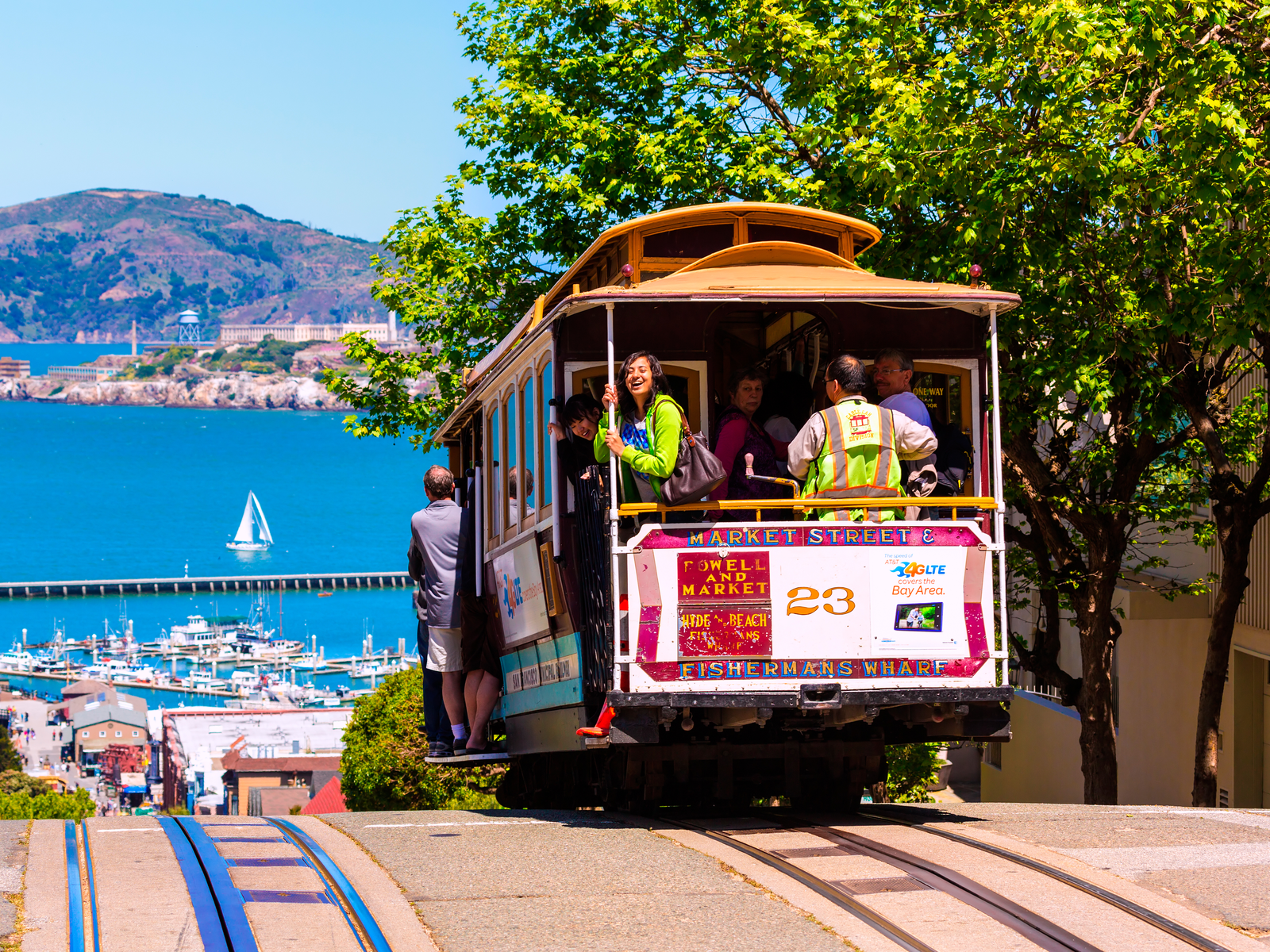 Tourists excitedly riding a cable car downhill at one of the best places to visit in San Francisco and a blue sea in background