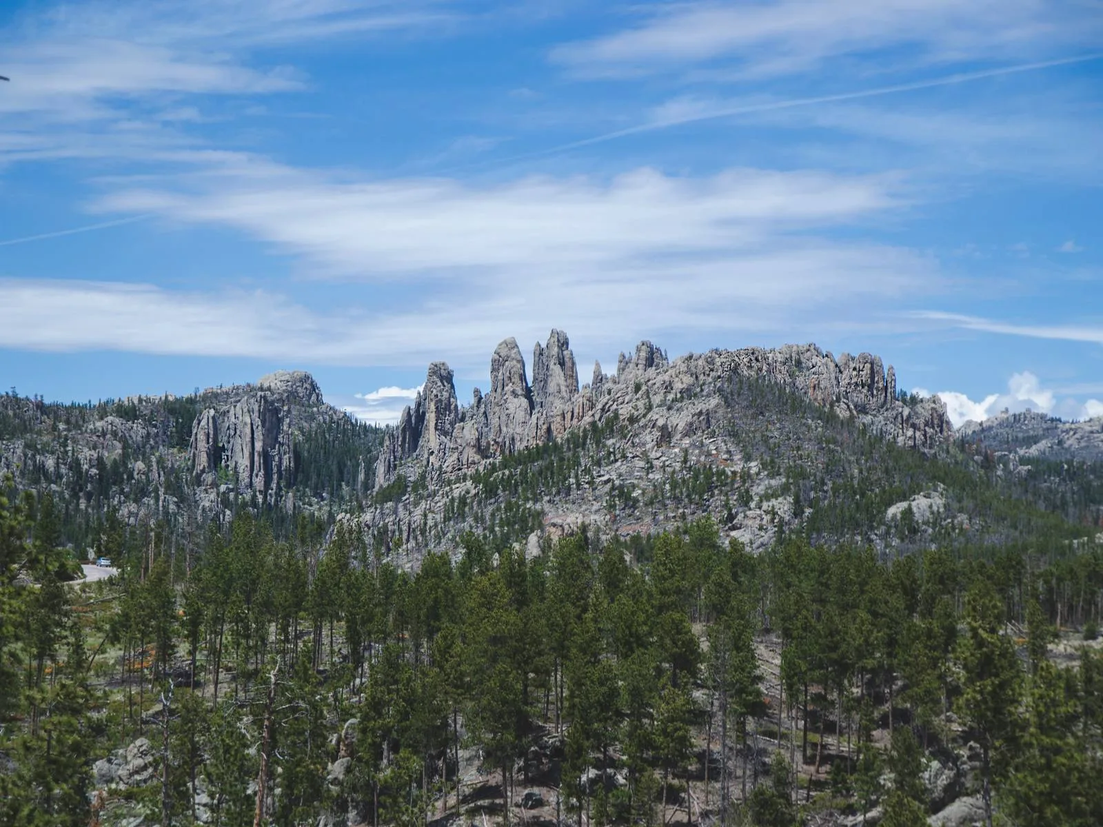 Black Hill's rocky mountains thin layers of pine trees pictured on a partly cloudy day as a piece on the best South Dakota tourist attractions