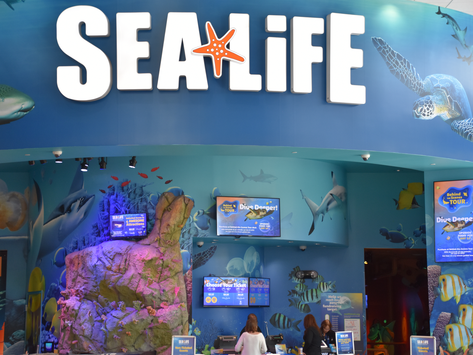 Two women buying tickets at marine-themed counter at SEA LIFE Orlando Aquarium, a piece on the best aquariums in Florida
