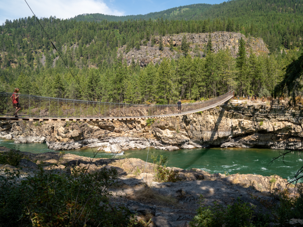 Two people traversing a hanging bridge crossing Kootenai River and their company on the other end at the Kootenai National Forest, one of the best things to see in Idaho