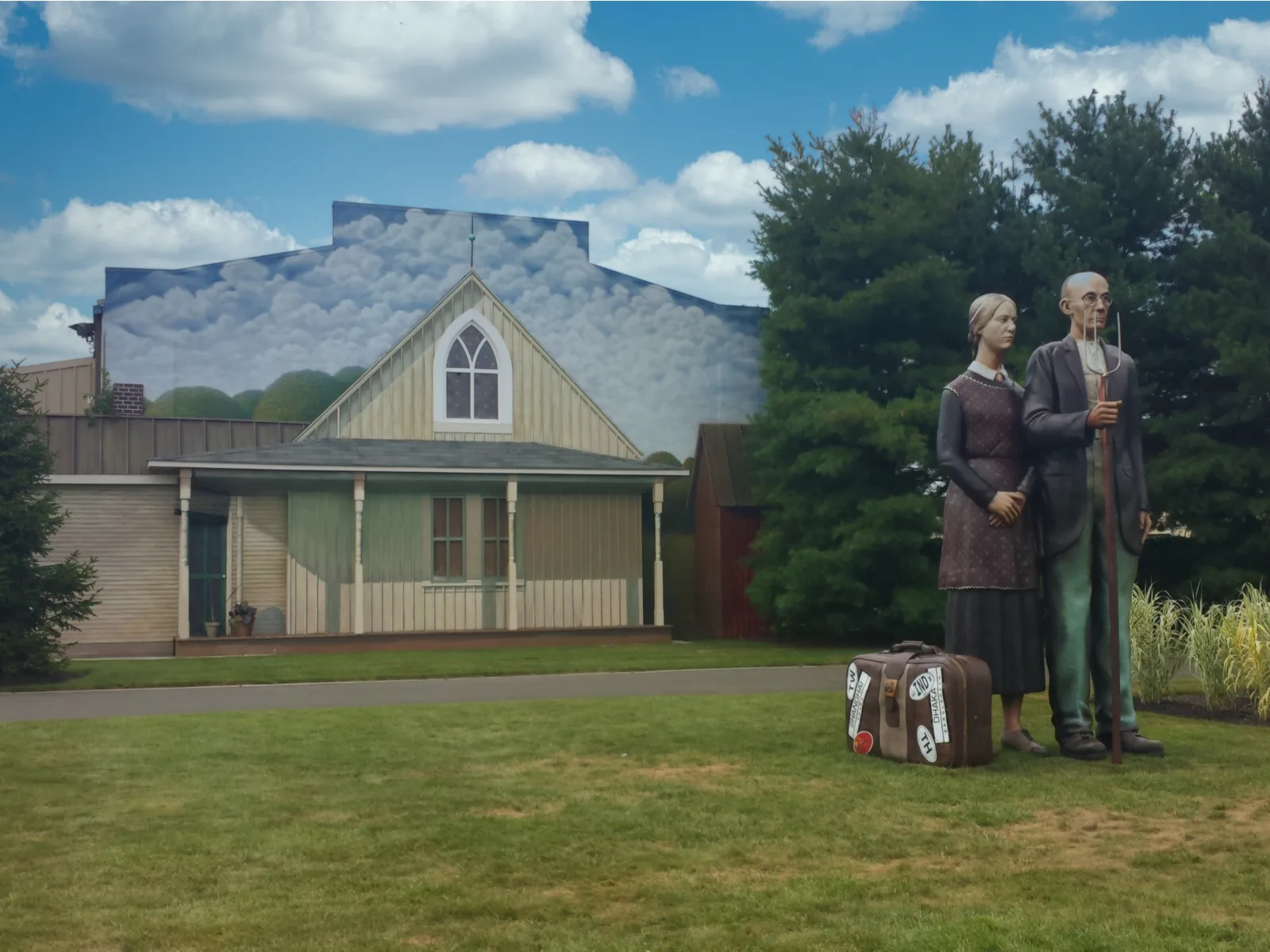 A sculpture of an old couple standing beside a luggage and holding a spading fork, entitled American Gothic Farmers, and viewing some other statues at the Grounds for Sculpture is one of the best things to do in New Jersey