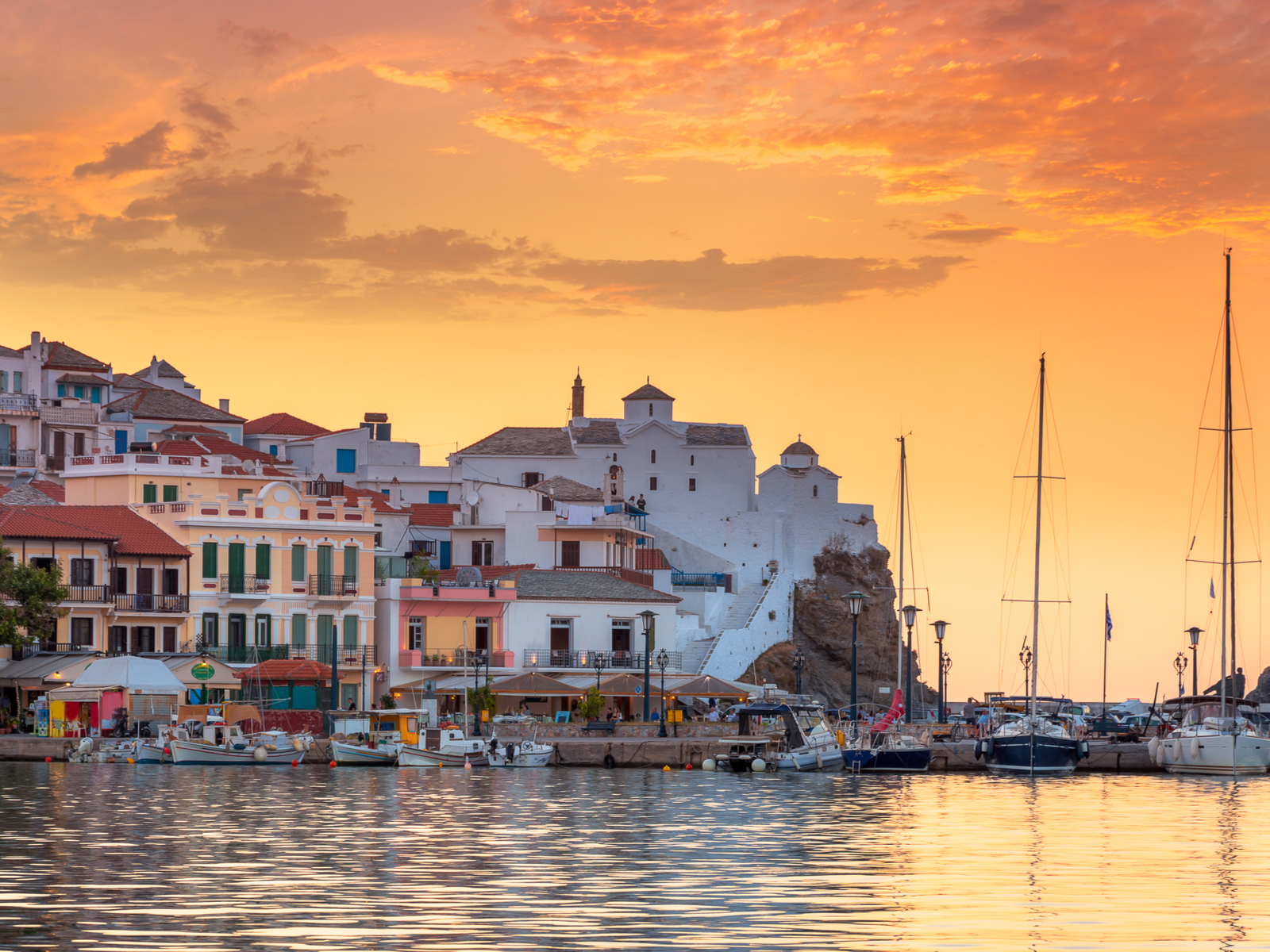 Stunning sunset over the Panagitsa Tou Pirgou Church and other structures beside the bay with docked fishing boats at Skopelos Island, one of the best places to visit in Greece