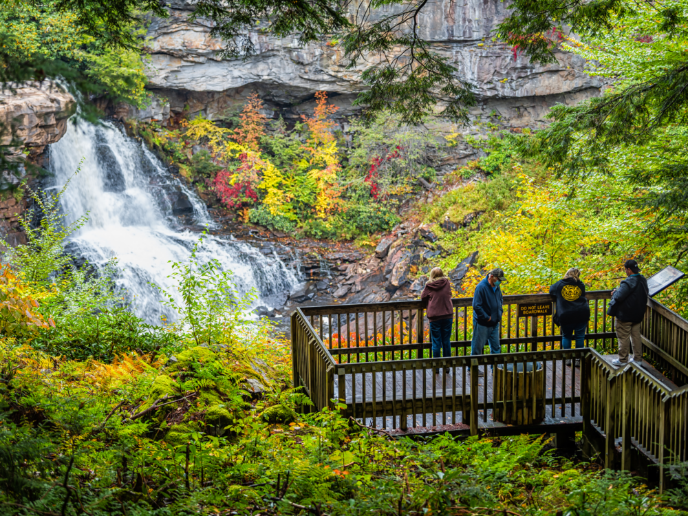 Four people in their jackets standing at the boardwalk of Blackwater Falls State Park, one of the best attractions in West Virginia, witnessing the waterfalls and surrounding greeneries