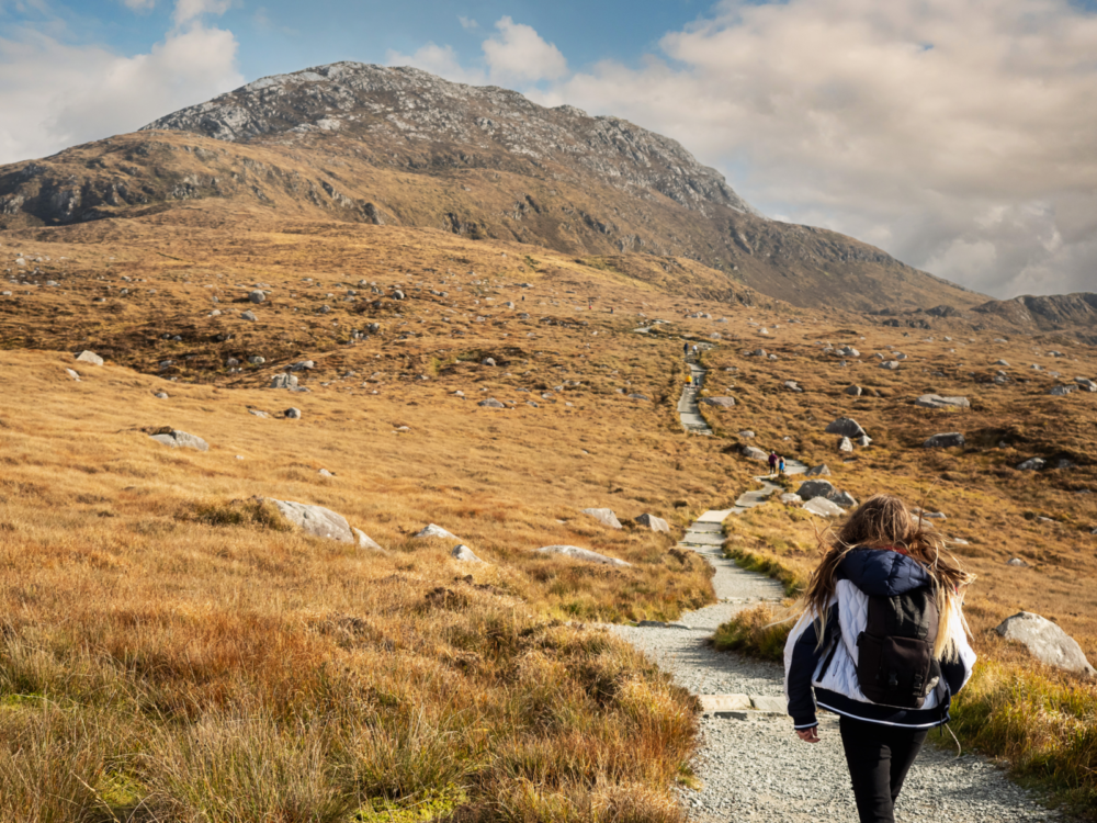 A girl on her jacket and black backpack trailing behind other hikers going up the Diamond Hill Loop, known as one of the best hikes in Ireland
