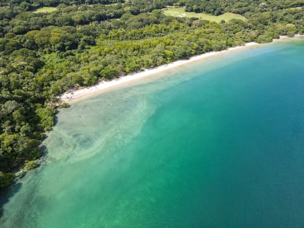 A straight white sand shore dividing the lush greenery and clear green waters of Playa Nacascolo, one of the best beaches in Costa Rica