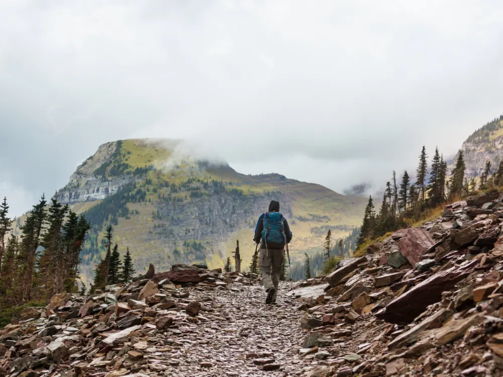 A man hiking a rocky trail in Glacier National Park, one of the best things to do in Montana, towards a misty peak mountain