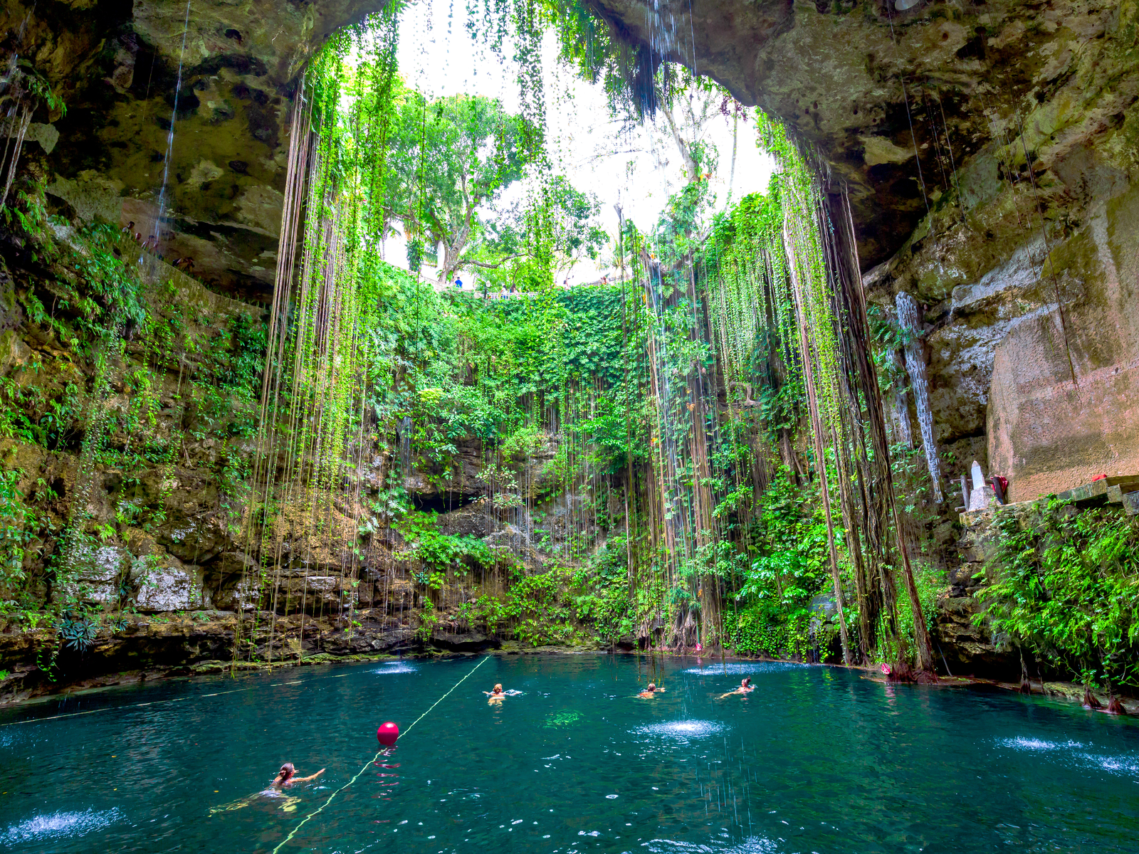 Tourist enjoying a swim at a gigantic well with dangling vines at its crater in Cenote Ik Kil as one of the best things to do in Cancun