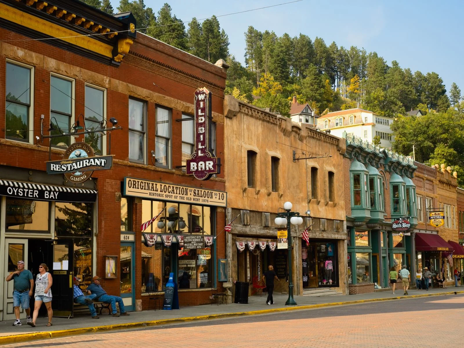 Locals and tourists on the sidewalk of Historic Deadwood, with the best South Dakota tourist attractions of historic saloons, bars, and shops