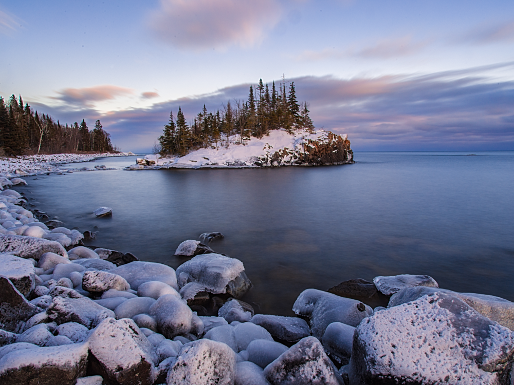 A rocky riverbank of Lake Superior in Wisconsin, one of the best lakes in the U.S., and a snow-covered island at dusk