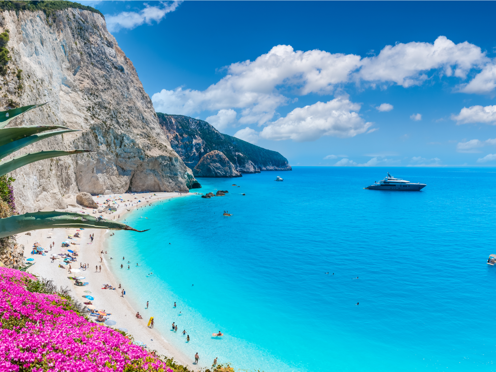 People enjoying the beautiful Porto Katsiki beach beside a tall cliff and cruise ship anchored offshore on Lefkada island, one of the best places to visit in Greece