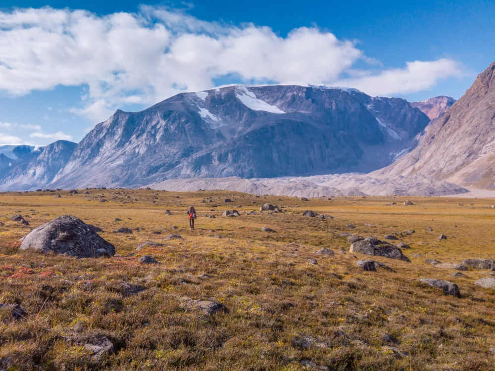 A lonely hiker passing through the rocky plains and icy mountain peaks of Akshayuk Pass in Baffin Island, one of the best places to visit in Canada