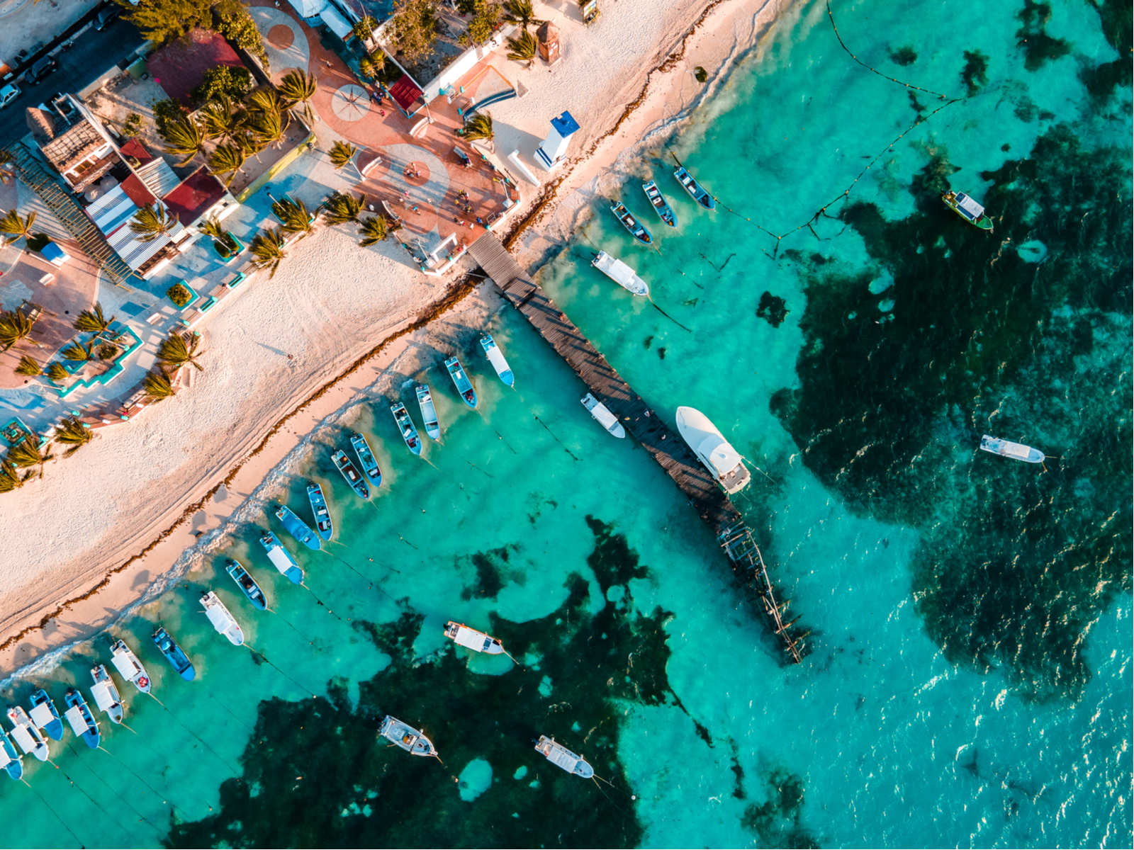 Overhead view on white sand Puerto Morelos Beach's, one of the best beaches in Cancun, anchored small boats on crystalline waters and a short boardwalk leading towards a resort