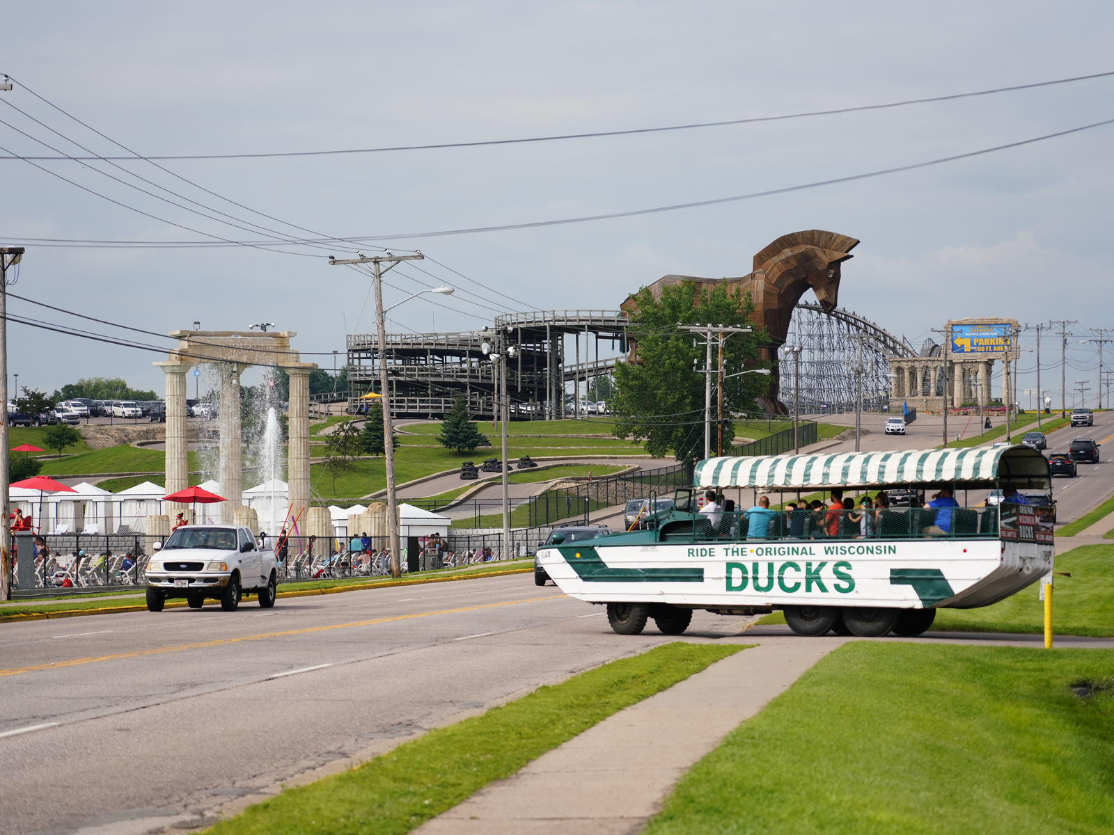 The six-wheel amphibious Wisconsin Ducks, one of the best Wisconsin tourist attractions, filled with passengers and crossing a road with a large trojan horse replica in background