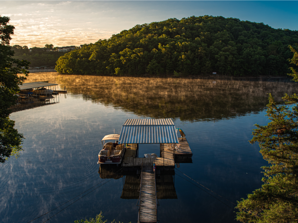 A calm early morning at Lake of the Ozarks in Missouri, one of the best lakes in the U.S., where a hill of trees and a small dock are reflected on its waters
