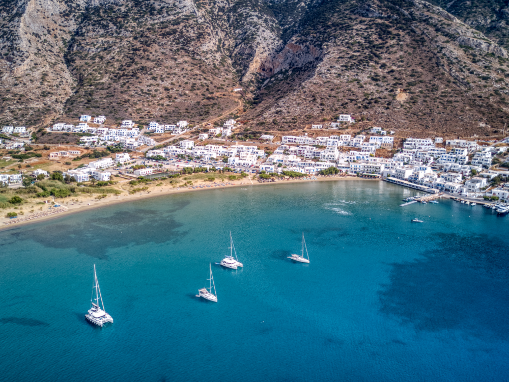 Aerial view on white coastal structures and sailboats anchored in the turquoise Kamares Bay on Sifnos island, in the list of the best places to visit in Greece