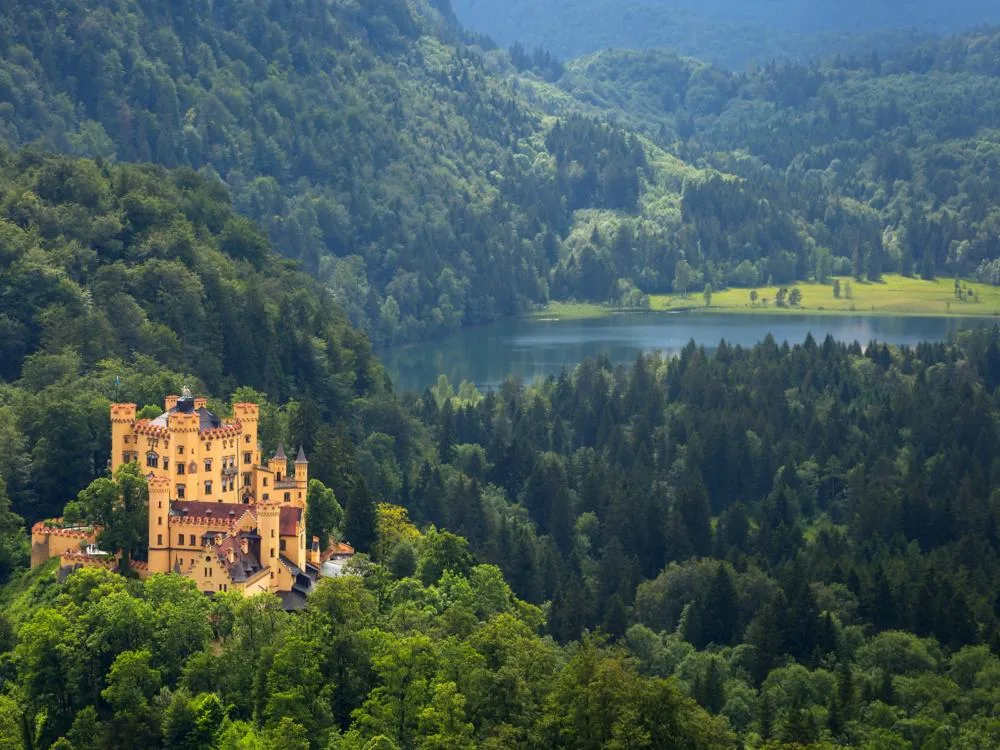 Situated in the of a dense forest in Balvarian Alps, one of the best castles in Germany, Hohenschwangau Castle's overlooking view of a calm river at a distance