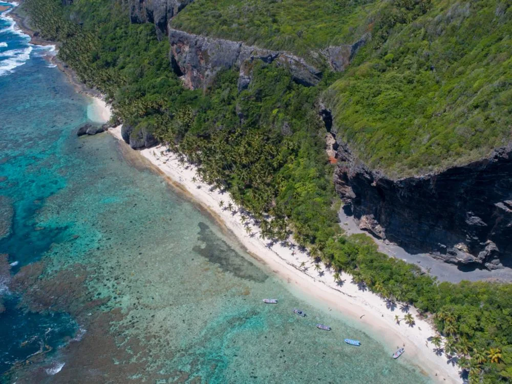 Overhead view of virgin Playa Fronton in Las Galeras sitting beside a lush greeneries and a tall cliff, one of the best beaches in the Dominican Republic, pictured with four small boats near the shore