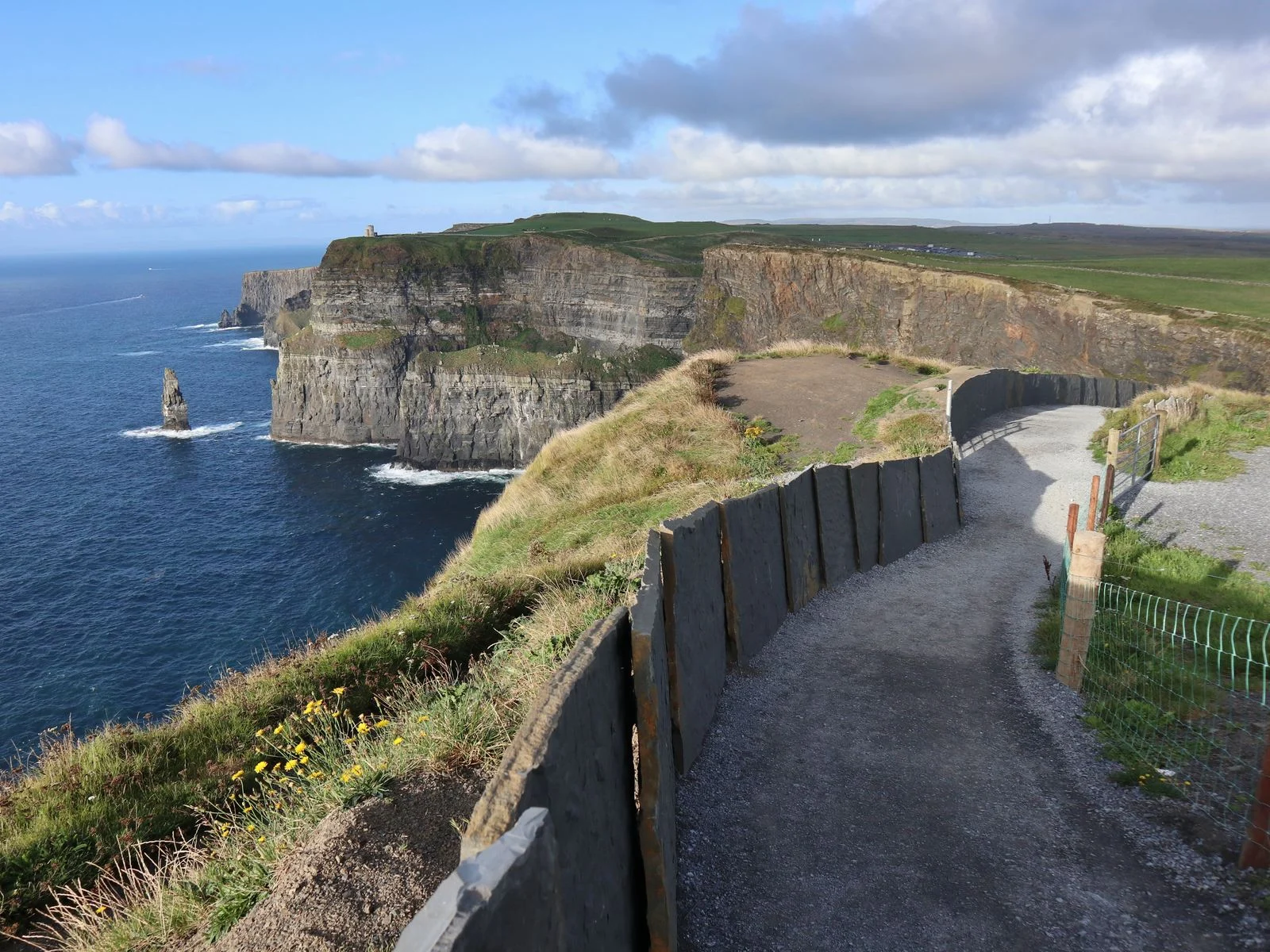 A barricaded path beside Cliffs of Moher, with calm sea, is one of the best hikes in Ireland