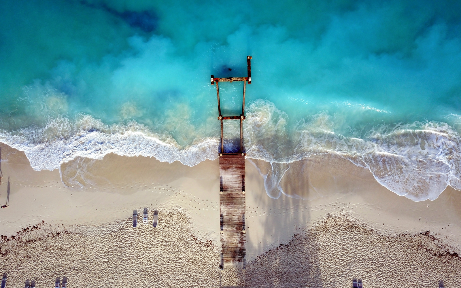 Drone shot of a dock on a beach with teal water outside the best resort in Turks and Caicos