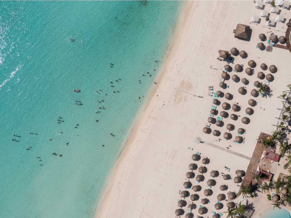 Aerial view on Playacar Beach, named as one of the best beaches in Cancun, its wide shore filed with native huts and a number of tourists swimming on the shallow crystal clear water