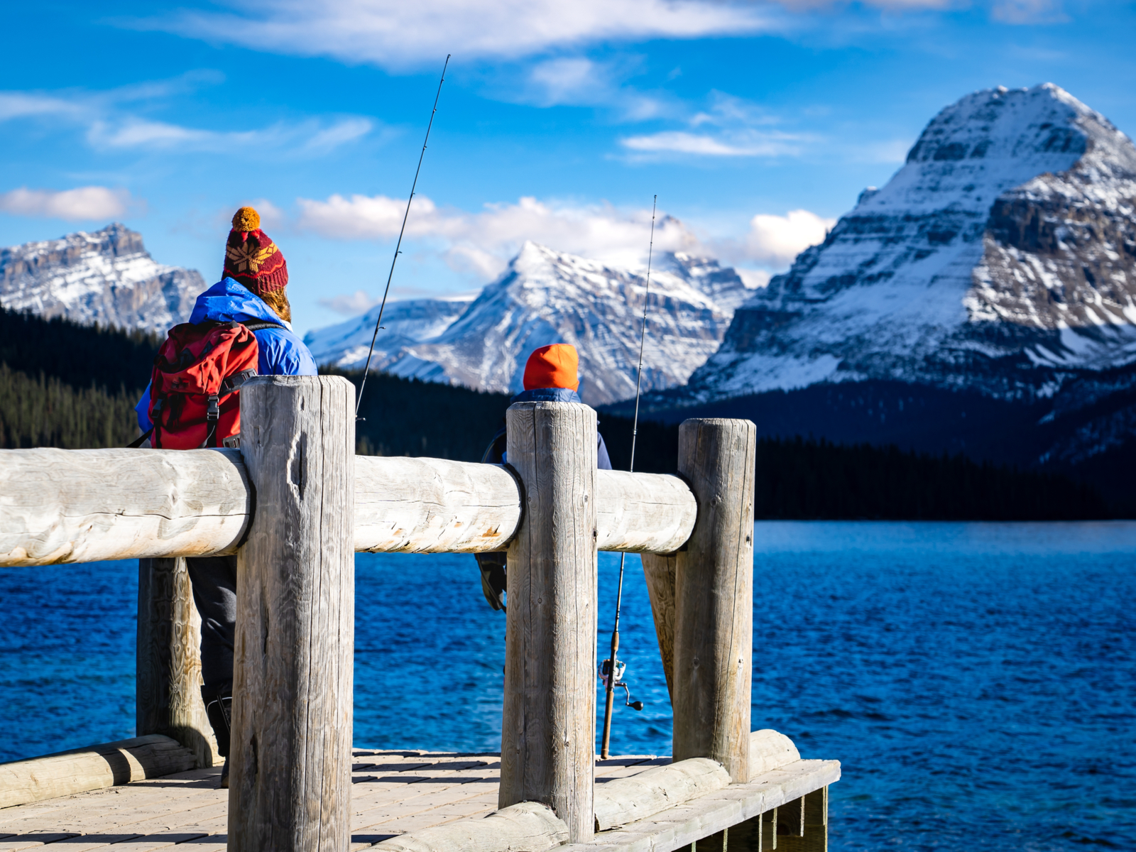 Dad and son fishing off a wooden dock during the least busy time to visit Glacier National Park