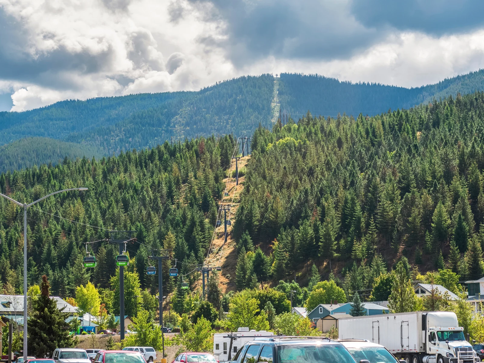 Cars parked at the foot of the Silver Mountain Resort and a ski lift gondola going up the mountain peak on a summer day, one of the best things to see in Idaho
