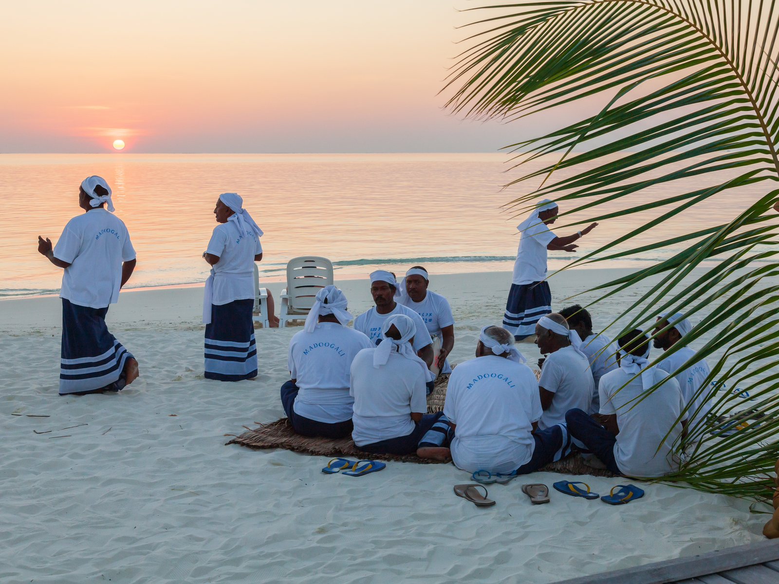 Maldivian locals in white dress sitting on a beach during the best time to visit Maldives