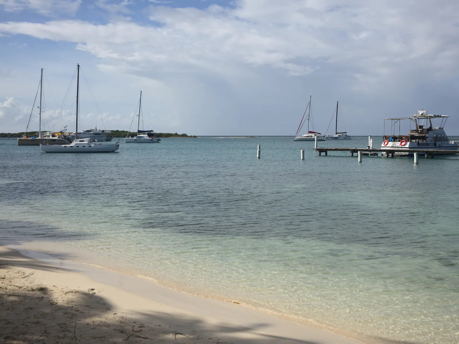 Several boats anchored and docked near the shore of Surfside Beach, one of the best beaches in Aruba, on a calm and cloudy weather