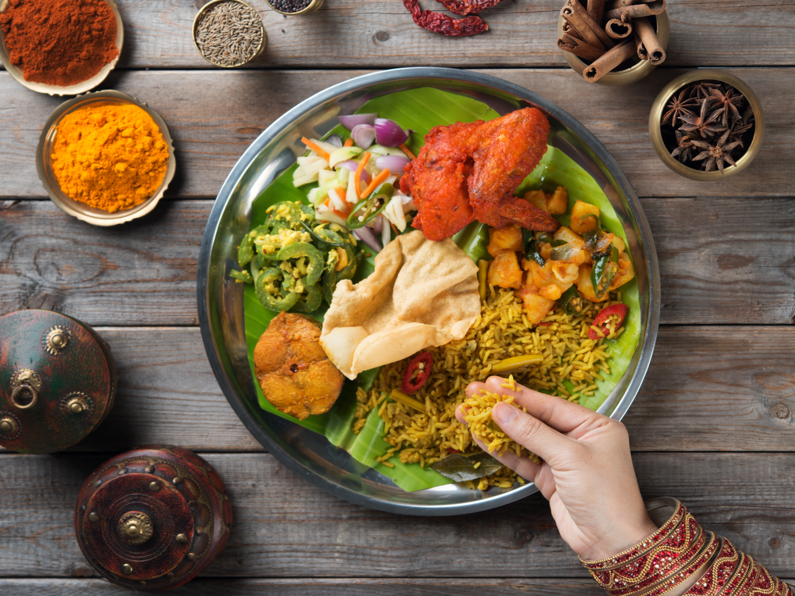 Overhead view of a person eating spices-encircled Biryani Rice by hand served on a wooden table at Spice of India, names as one of the best restaurants in St. Lucia