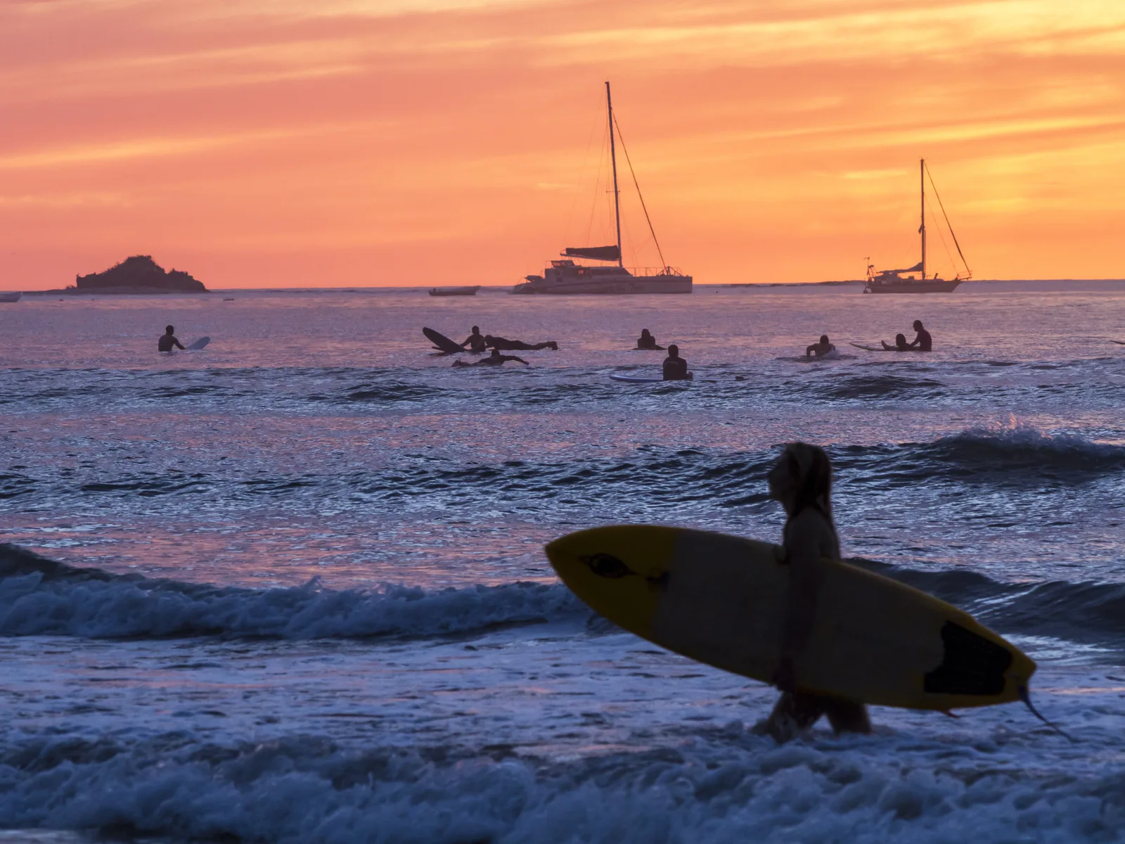 Silhouette of boats and surfers paddling during the sweet sunset at Tamarindo Beach, a piece on the best beaches in Costa Rica
