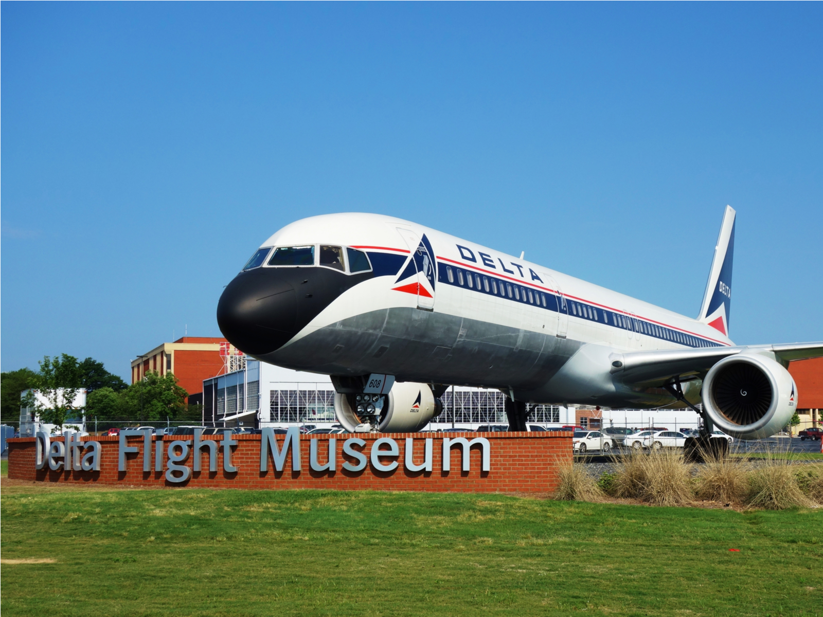 A large white passenger plane displayed behind Delta Flight Museum's, one of the best tourist attractions in Georgia, signage fronting a green landscape