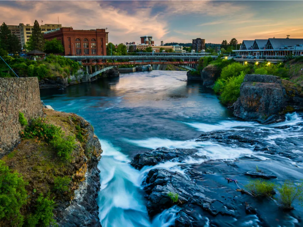 One of the best places to visit in Washington State, Spokane Falls in the middle of the city below a bridge at dusk