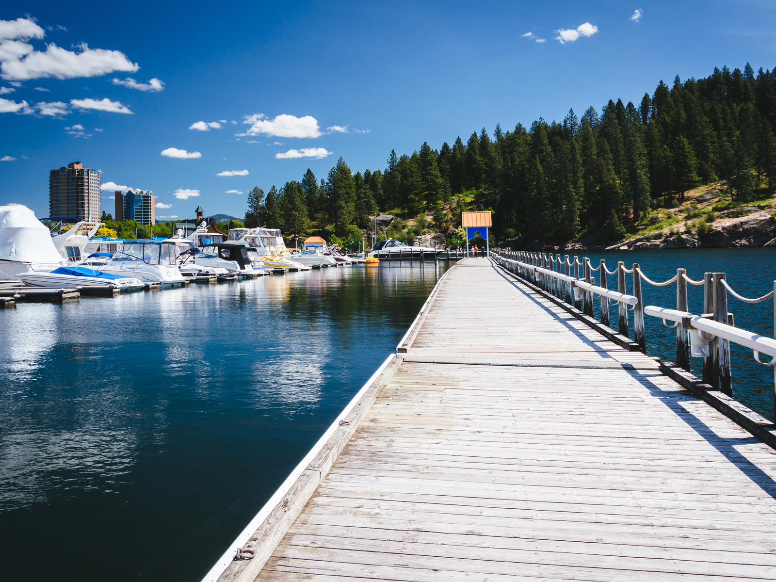 Three people standing on the end of a board walk and several boats docked at the calm Lake Coeur d' Alene, one of the best things to see in Idaho