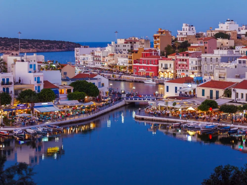 Populated Agios Nikolaos City reflected on the calm Voulismeni Lake at dusk in Crete, a piece on the best places to visit in Greece