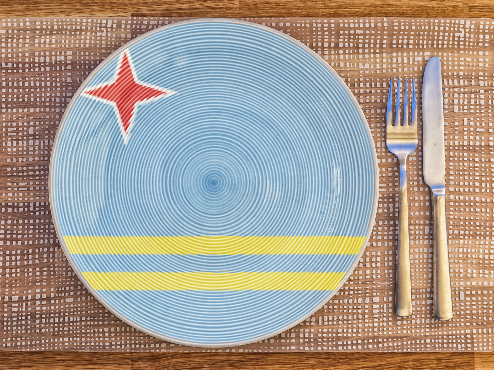 Photo of a dinner plate with the Aruban flag on the plate and silverware for a roundup of the best restaurants in Aruba