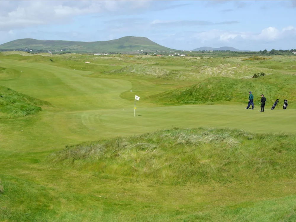 Two golfers walking towards a white flag at the vast golf course of Waterville Golf Links, one of the best golf courses in Ireland