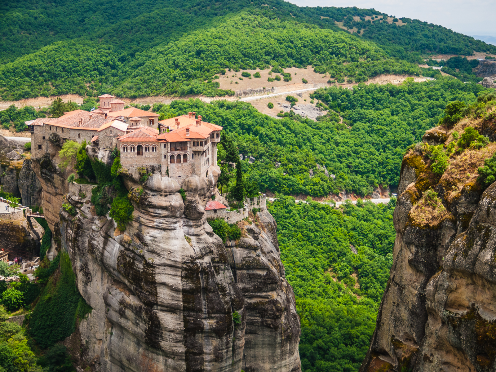 Aerial view on the Meteora as one of the best places to visit in Greece where monasteries structures sit atop the grand rock formation and at the bottom is lush forest