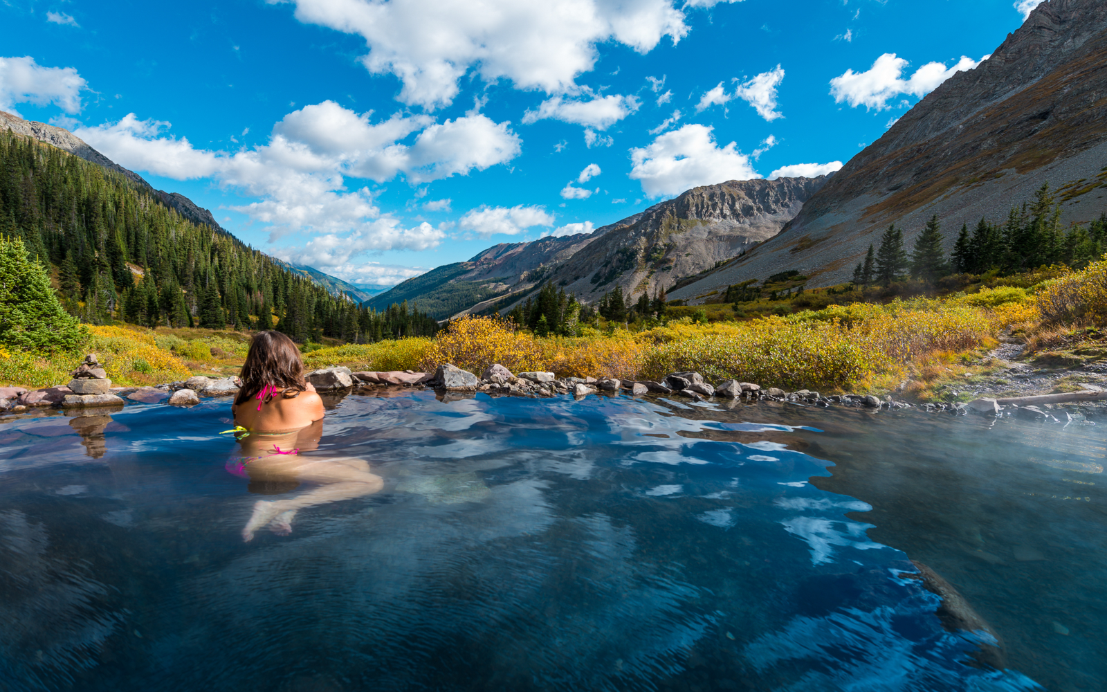 Woman sitting in the Conundrum water, one of the best hot springs in Colorado, looking at the Aspen mountain range